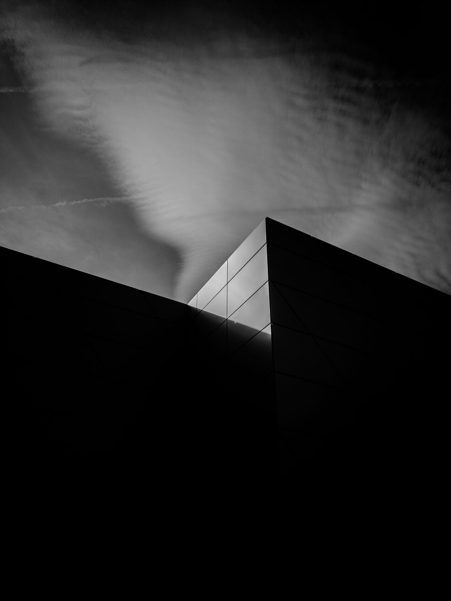 The corner of a dark building against a clouded sky
