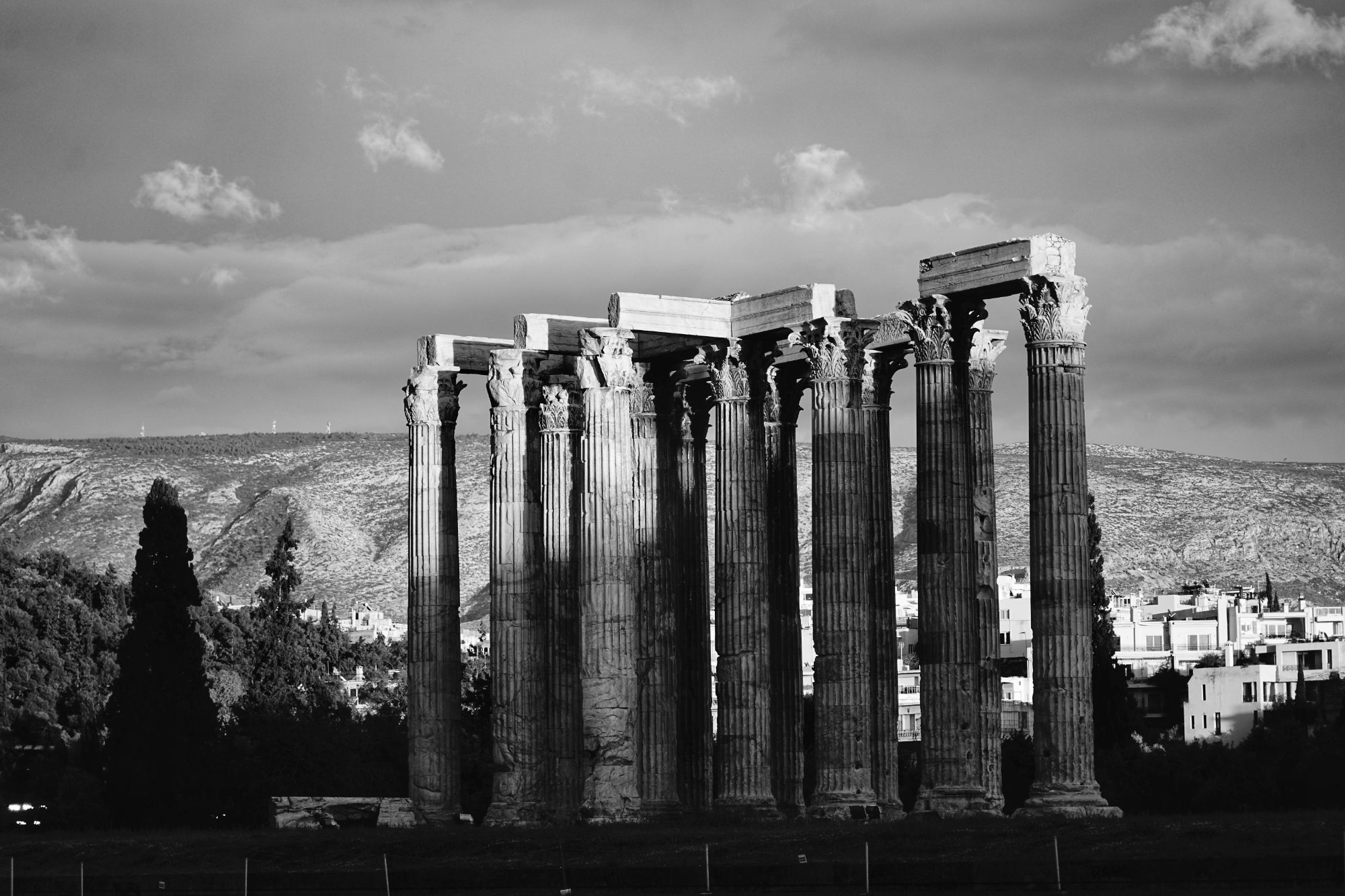 The standing columns of a classical temple against a cloudy sky, in black and white