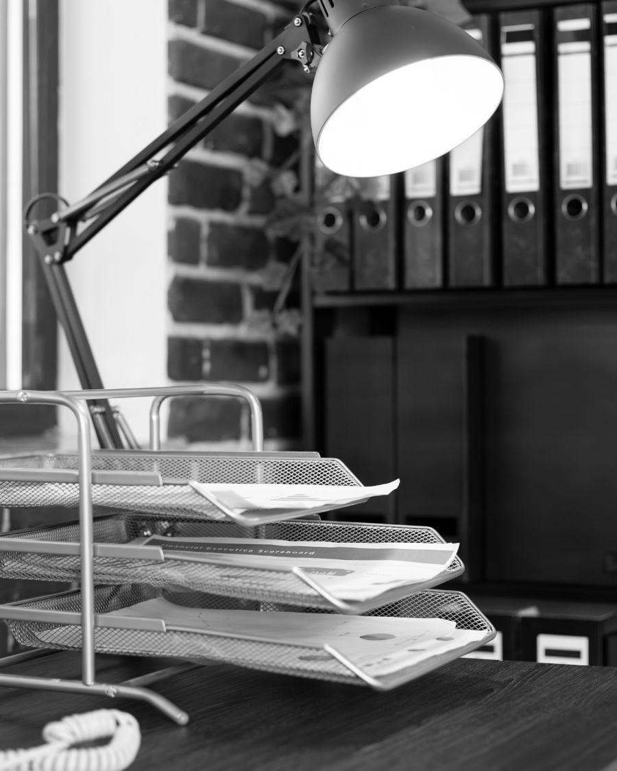 An empty office desk with a lamp, letter trays and ring binders