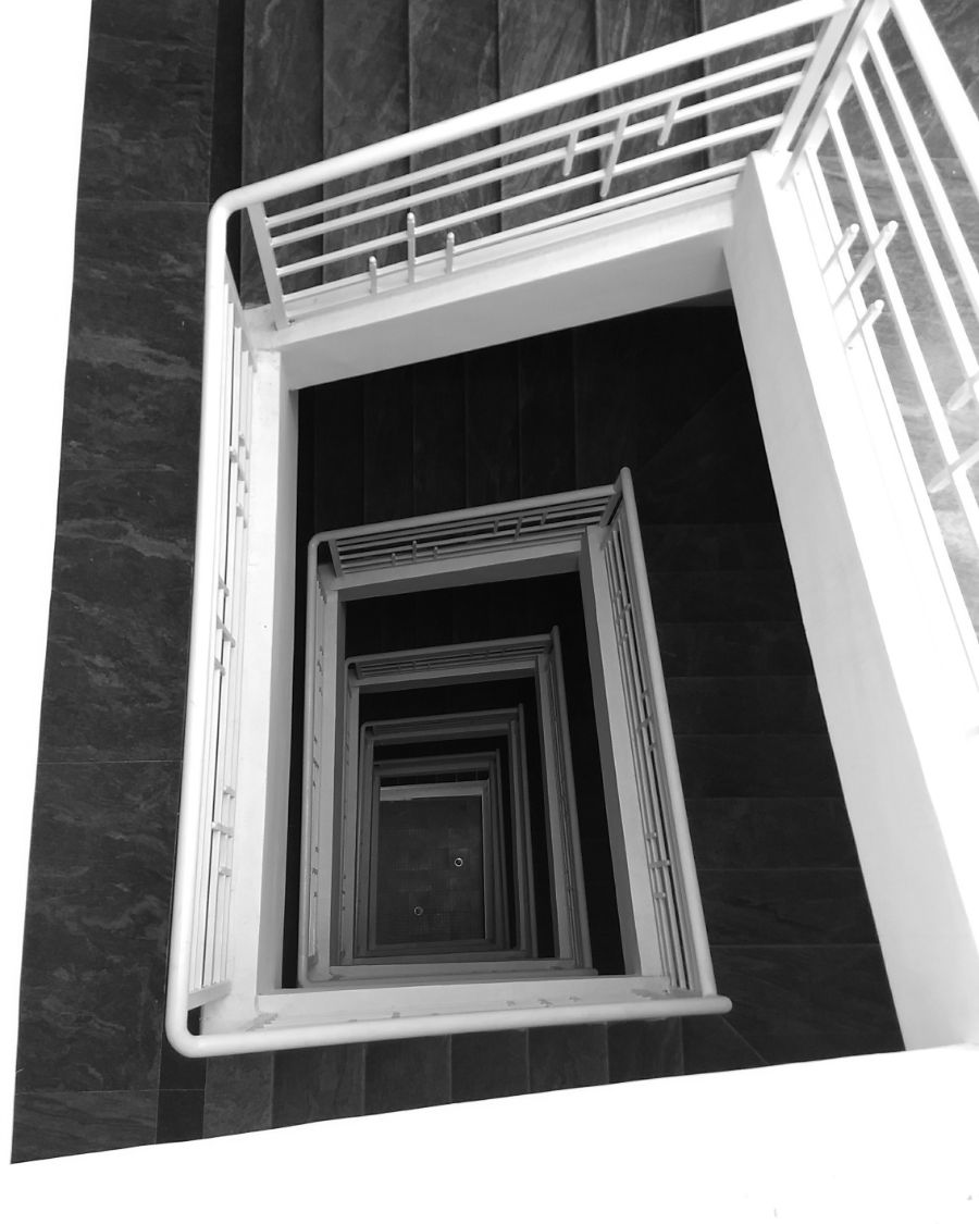 A white square stairwell descending through a dark stone building