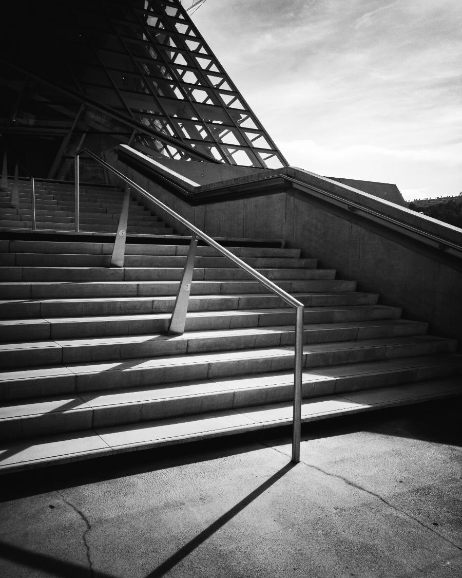 Broad outdoor steps with a steel handrail under a lattice roof