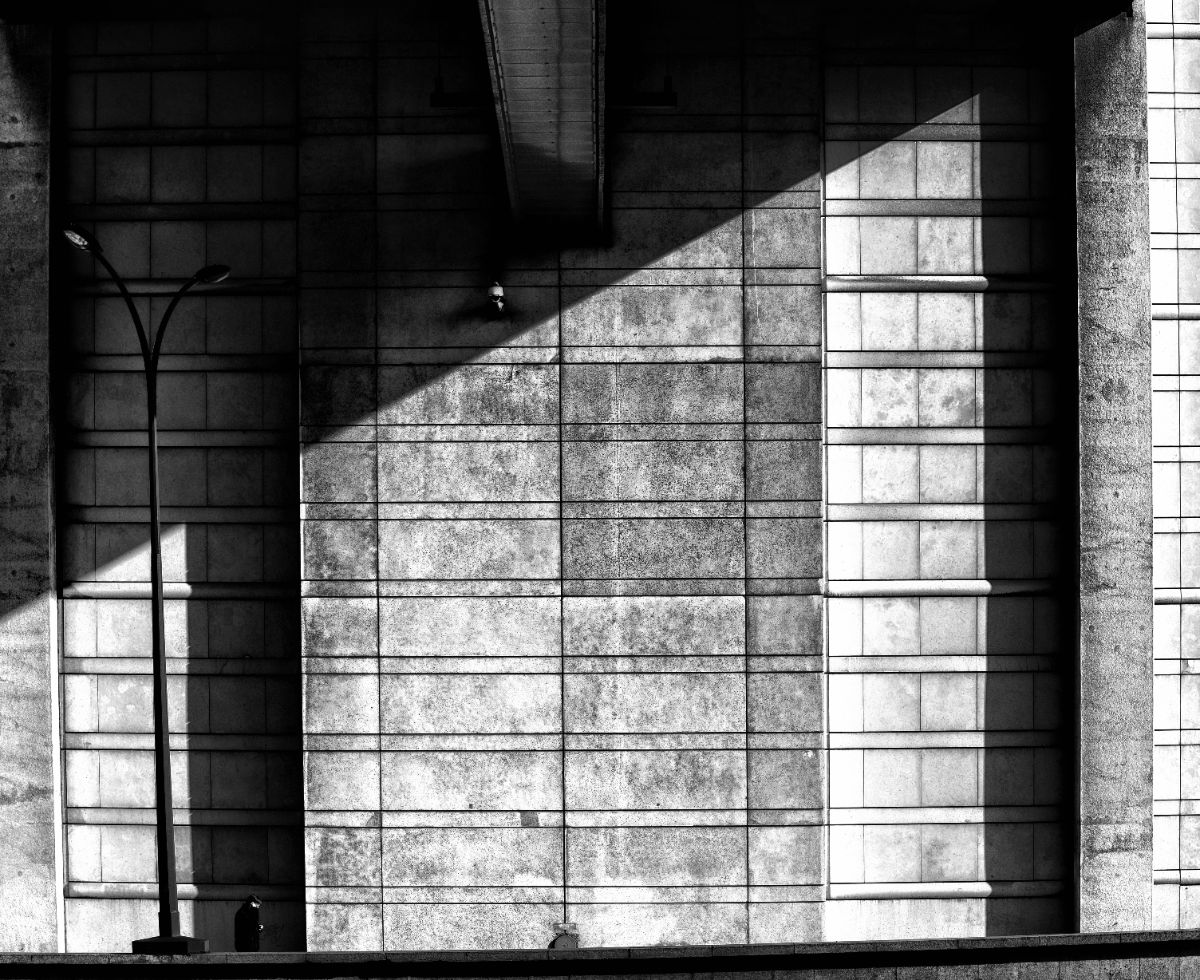 A shaft of light across a stone wall beside a single street lamp