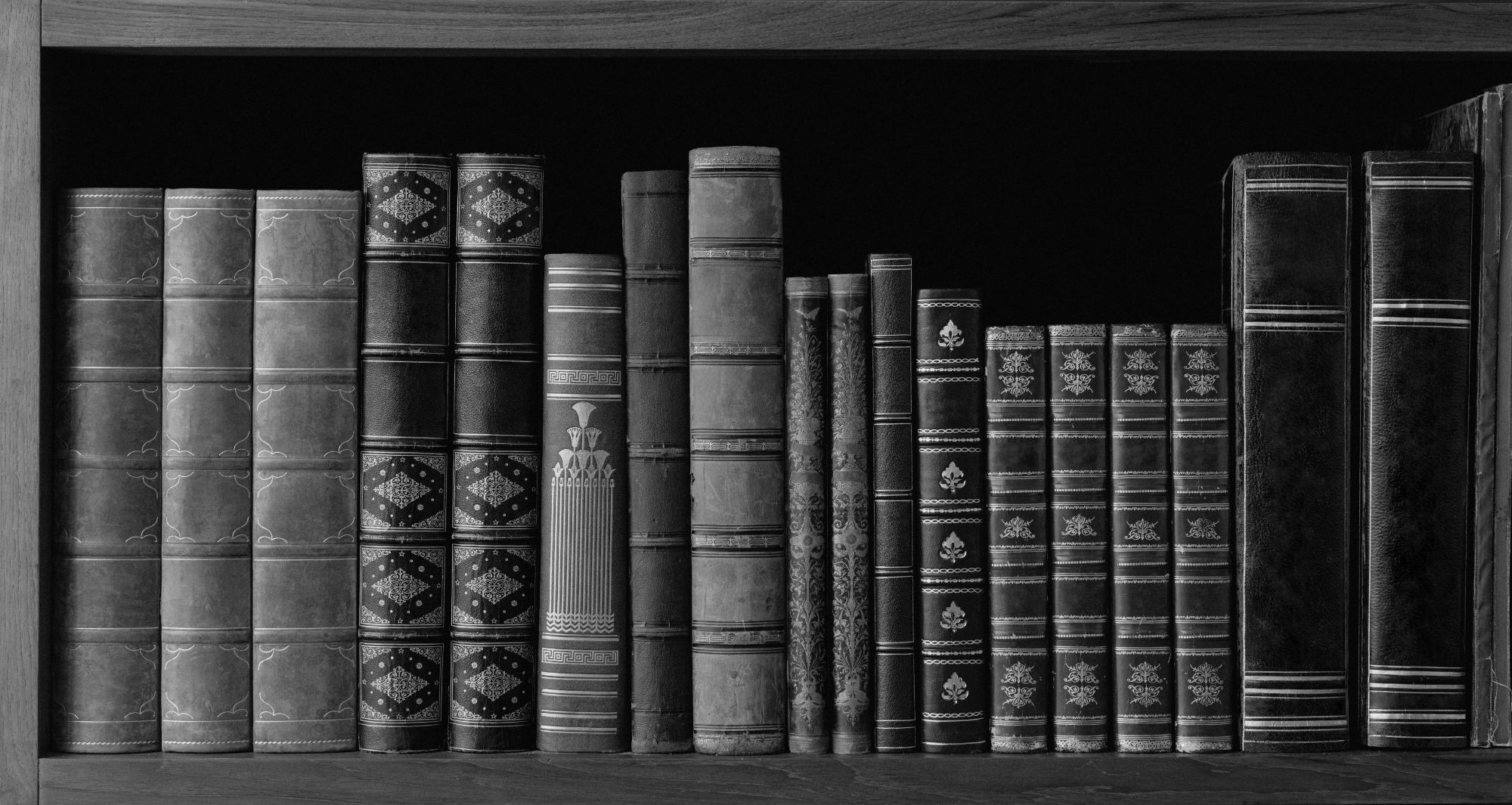 A row of leather-bound antique books on a dark shelf