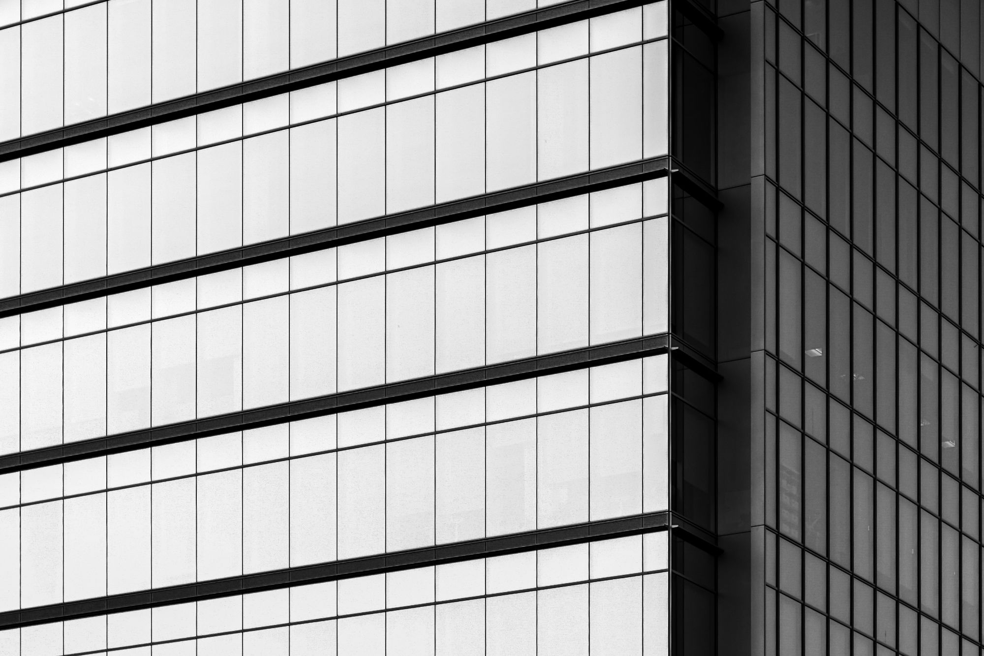 A glass curtain wall with horizontal bands, meeting a gridded facade at a corner